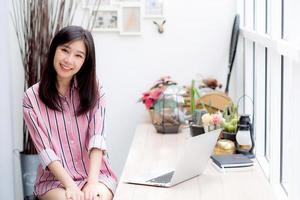 mooi van portret aziatische jonge vrouw die online werkt op een laptop die in de coffeeshop zit, professionele vrouwelijke freelancer die een notebookcomputer gebruikt met verbinding met internet voor een baan op afstand. foto