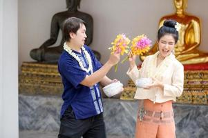 jonge thaise mannen en vrouwen in traditionele thaise kleding houden bloemen opspattend water voor de lol op het songkran waterfestival foto