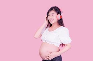 Aziatische mooie zwangere vrouw staat ontspannen en luistert graag naar muziek op een koptelefoon die is aangesloten op internet foto