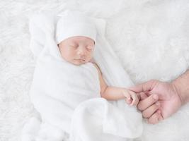 pasgeboren babymeisje slaapt warm op de witte doek en raakte haar vaders hand met liefde aan foto