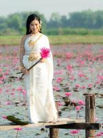 een elegante thaise vrouw die traditionele thaise kleding draagt met lotusbloemen verzameld uit een lotusveld foto