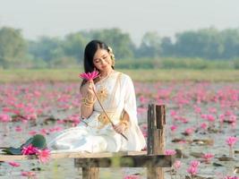 een elegante thaise vrouw die traditionele thaise kleding draagt met lotusbloemenblad verzameld uit een lotusveld foto