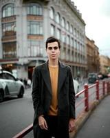 knappe stijlvolle modieuze man, brunette in elegante grijze jas, staat op straat in het historische centrum van st. petersburg. jonge man met donker haar, dikke wenkbrauwen. foto