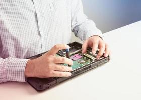 man repareert computer. een servicemonteur in shirt repareert laptop, aan een wit bureau tegen een witte muur. foto