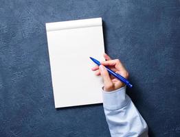 vrouw schrijft in notitieboekje op donkerblauwe tafel, hand in shirt met potlood, schetsboek tekenen foto