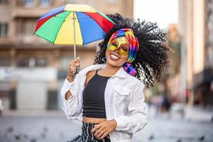 jonge vrouw met krullend haar viert het braziliaanse carnavalsfeest met frevo-paraplu op straat. foto