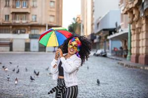 jonge vrouw met krullend haar viert het braziliaanse carnavalsfeest met frevo-paraplu op straat. foto