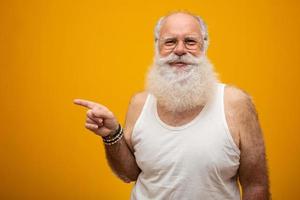 oude man met een lange baard die op een gele achtergrond wijst. senior met volle witte baard. oude man met een lange baard van verdriet. foto