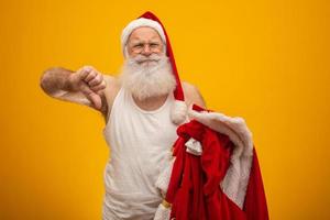 ongelukkige kerstman die zijn kleren vasthoudt na of voor het bezorgen van cadeautjes. kleding van de kerstman. kostuum. duim omlaag. foto