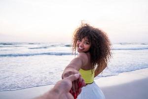 meisje met mannenhand en draait op tropisch exotisch strand naar de oceaan. volg mij shot van een jonge vrouw die haar vriendje aan de kust trekt. zomervakantie of vakantie. gezichtspunt