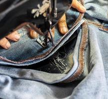 een close-up hand repareert de jeans met een oude naaimachine. foto