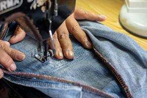 een close-up hand repareert de jeans met een oude naaimachine. foto