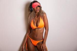 aantrekkelijk krullend haar meisje in een oranje bikini, hoed, emotioneel geopende mond op een witte achtergrond met een perfect lichaam. geïsoleerd. studio opname. foto