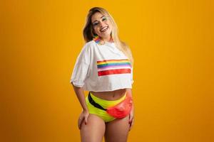 jonge blonde haarvrouw in kostuum die van het carnavalsfeest geniet dat bedekt is met lgbt-trots-t-shirt. alleen. een. lhbt-vlag. LGBT-symbool op gele achtergrond. foto