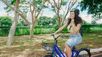 jonge latijnse vrouw in beschermende helm rijdt op haar fiets langs het fietspad in een stadspark foto