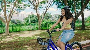 jonge latijnse vrouw in beschermende helm rijdt op haar fiets langs het fietspad in een stadspark foto