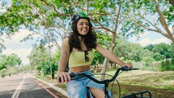 jonge latijnse vrouw in beschermende helm rijdt op haar fiets langs het fietspad in een stadspark foto