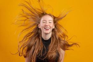 portret van mooie vrolijke roodharige meisje met vliegende haren lachend lachen camera kijken over gele achtergrond. foto