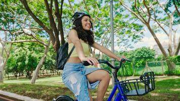 jonge latijnse vrouw in beschermende helm rijdt op haar fiets langs het fietspad in een stadspark foto