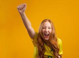 brazilie aanhanger. braziliaanse roodharige vrouw fan vieren op voetbal, voetbalwedstrijd op gele achtergrond. braziliaanse kleuren. foto