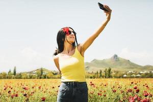 mooie blanke vrouw pose selfie met smartphone in de natuur voor sociale media buitenshuis op lente. gelukkig portret van vrouw in bloemenveld foto