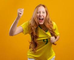 brazilie aanhanger. braziliaanse roodharige vrouw fan vieren op voetbal, voetbalwedstrijd op gele achtergrond. braziliaanse kleuren. foto