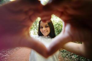 schattig gelukkig tienermeisje dat hartvorm handgebaar maakt kijkend naar de camera, grappig glimlachend etnisch jonge alleenstaande vrouw blogger lachend gezicht met liefdesteken symbool, park, close-up portret foto