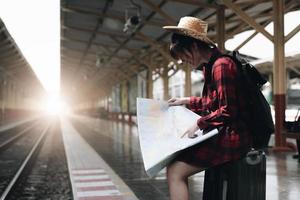 jonge reizigersvrouw die op kaarten kijkt die reis plannen bij treinstation. zomer en reizen lifestyle concept foto