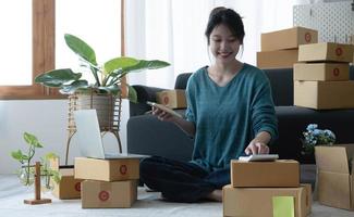 Aziatische vrouwen schrijven een notitie van bestellingen van goederen met een lachend gezicht in het concept van het MKB, e-commerce business foto