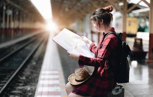 mooie jonge reizigersvrouw die op kaarten kijkt die reis plannen bij openbaar treinstation. zomer en reizen lifestyle concept foto