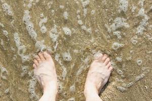 Aziatische blanke mannelijke voeten op het zand met een golf komt binnen, op vakantie. kopieer ruimte. bovenaanzicht foto