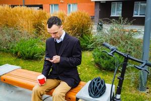 jonge mannelijke zakenman met fiets en kopje koffie of thee buiten wandelen foto
