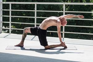 jonge man met tatoeages doet yoga-oefeningen buiten op balkon foto