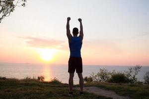 fit mannelijke hardloper training op het zomerstrand en luister naar muziek tegen prachtige lucht en zee foto