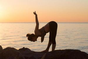 fitness gemengd ras aziatische vrouw in yoga pose op het ochtendstrand, mooie fit vrouw praktijk fitness exrxise stenen, ochtend zee of oceaan achtergrond foto