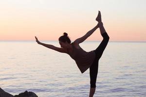 fitness gemengd ras aziatische vrouw in yoga pose op het ochtendstrand, mooie fit vrouw praktijk fitness exrxise stenen, ochtend zee of oceaan achtergrond foto