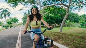 jonge latijnse vrouw in beschermende helm rijdt op haar fiets langs het fietspad in een stadspark foto