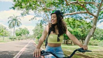 jonge latijnse vrouw in beschermende helm rijdt op haar fiets langs het fietspad in een stadspark foto