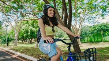 jonge latijnse vrouw in beschermende helm rijdt op haar fiets langs het fietspad in een stadspark foto