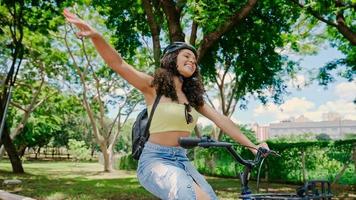 jonge latijnse vrouw in beschermende helm rijdt op haar fiets langs het fietspad in een stadspark foto