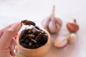 hand met gefrituurde krekels als eetbare insecten met een hoog eiwitgehalte in houten strik met kruidenachtergrond foto
