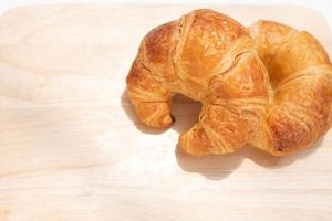 croissant geïsoleerd op houten plaat, vers gebakken brood voor eenvoudig ontbijt. foto