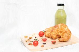 croissant met rode tomaten geïsoleerd op houten plaat, vers gebakken brood voor eenvoudig ontbijt. foto