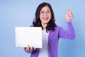 portret van een Aziatische vrouw van middelbare leeftijd die laptop op blauwe achtergrond gebruikt foto