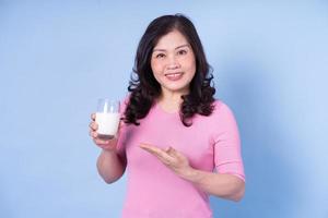 afbeelding van een Aziatische vrouw van middelbare leeftijd die melk drinkt op een blauwe achtergrond foto