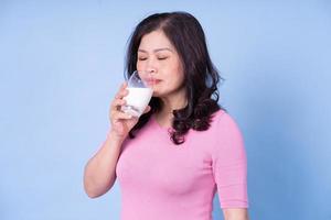 afbeelding van een Aziatische vrouw van middelbare leeftijd die melk drinkt op een blauwe achtergrond foto