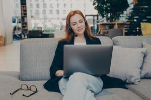 jonge vrouw die als callcenteragent online werkt met behulp van draadloze oortelefoons, headset en laptop foto