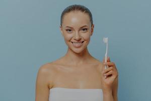 mondhygiëne. gelukkige jonge vrouw die tanden poetst na het douchen, glimlachende vrouw die tandenborstel vasthoudt foto