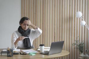 vermoeide dame freelancer zit aan bureau op kantoor aan huis ziekelijk kijkend naar digitale thermometer foto