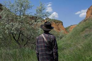 achteraanzicht van jonge mannelijke wandelaar in cowboyhoed buiten wandelen in zomerdag. hipster reiziger. foto